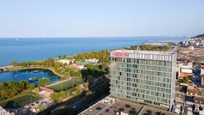 Et moderne hotel med stor glasfacade, beliggende nær et vandareal og et sportskompleks.