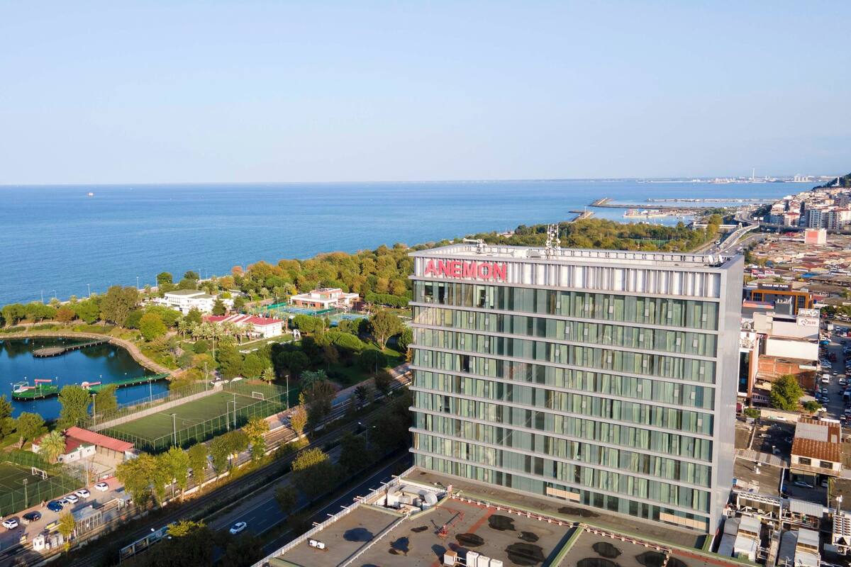 Un hôtel moderne doté d’une grande façade en verre, situé près d’un plan d’eau et d’un complexe sportif.