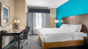 A hotel room with a large bed, a desk with a chair, a telephone, and a lamp.