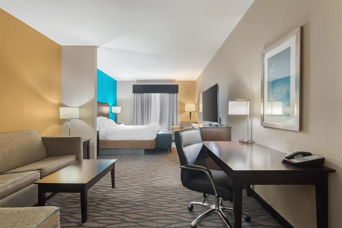 A hotel room with a bed, a desk, a chair, a sofa, a TV, and a phone.
