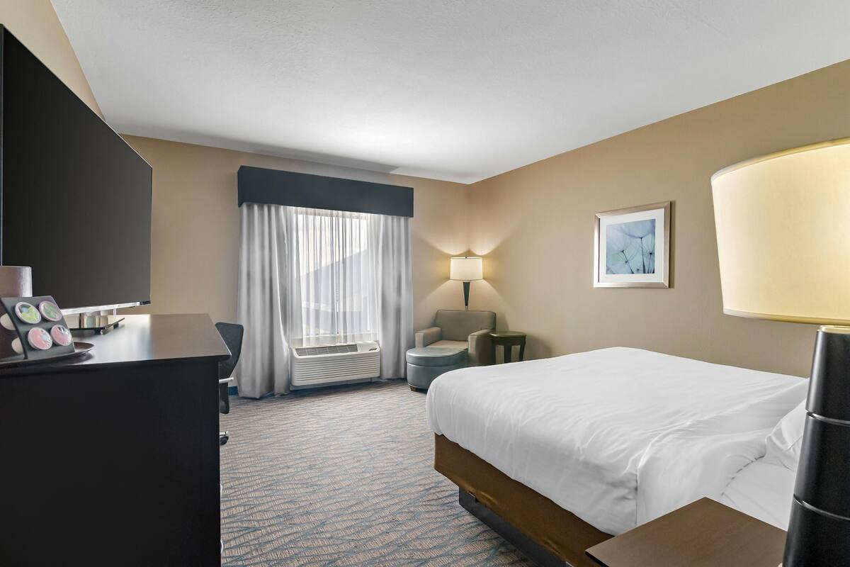 A hotel room with a bed, desk, chair, lamp, and artwork.