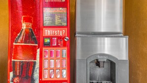 A Coca-Cola vending machine with a large Coca-Cola bottle image and a menu board. - Budget Inn and Suites (Crowley)