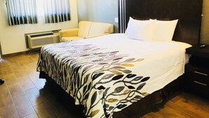 A hotel room with a large bed, a chair, a bedside table, and a window with curtains. - Budget Inn and Suites (Crowley)