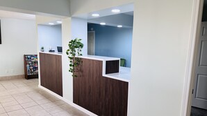 A reception area with a wooden reception desk, a potted plant, a bulletin board, and a blue wall. - Budget Inn and Suites (Crowley)