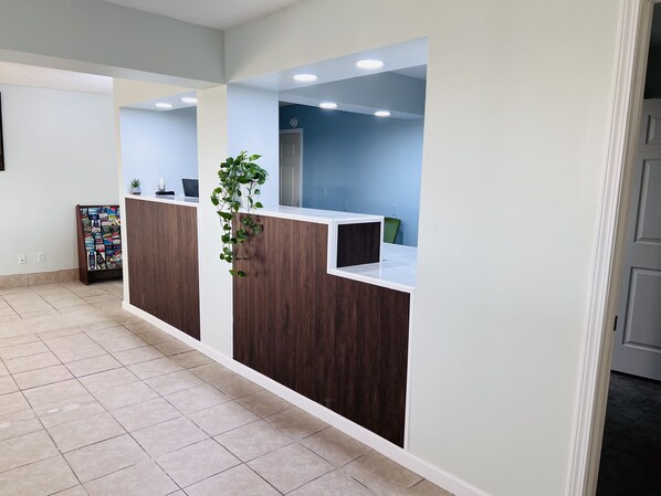 Een receptiehoek met een houten receptiebalie, een potplant, een prikbord en een blauwe wand.