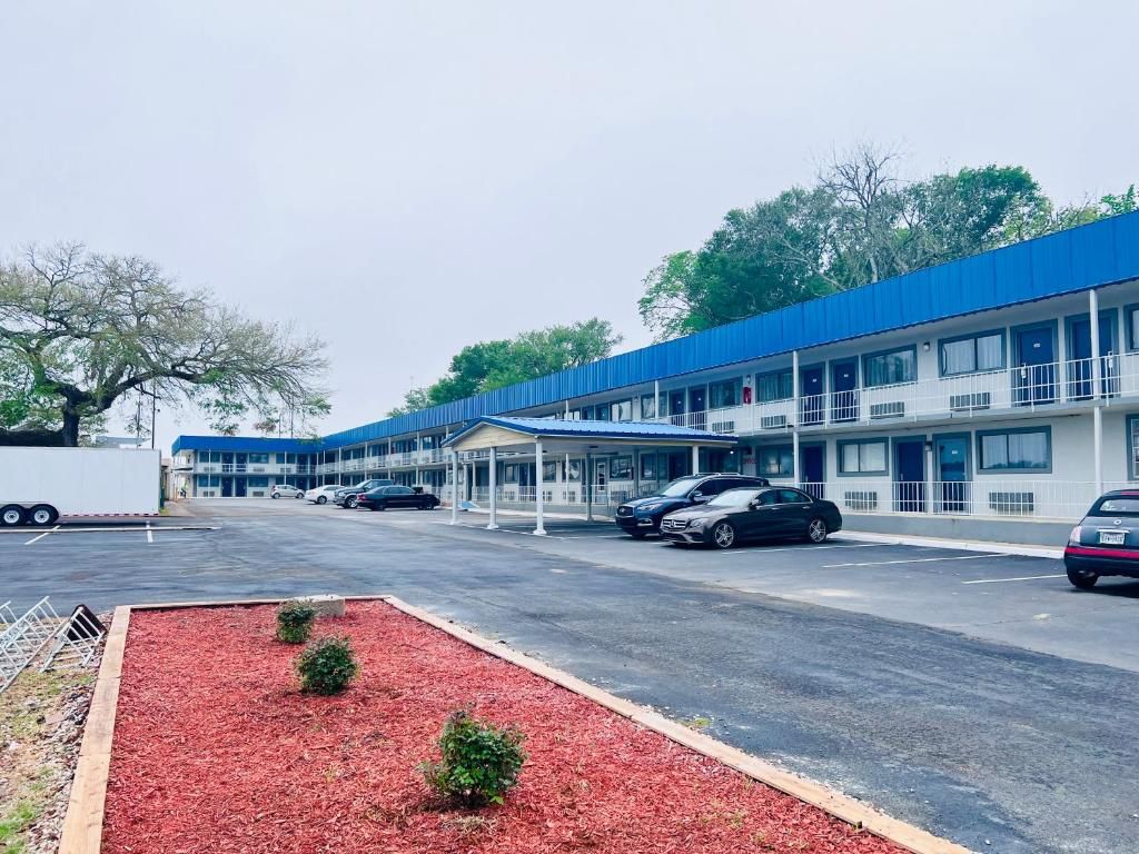 Un motel con varias habitaciones, zona de estacionamiento techada y un área ajardinada de color rojo.