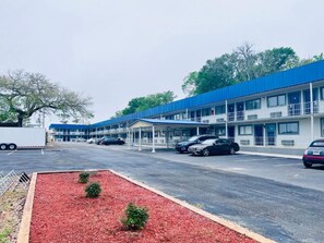 A motel with multiple rooms, a covered parking area, and a red landscaped area. - Budget Inn and Suites (Crowley)