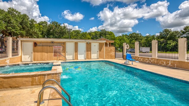 A swimming pool with a wooden building in the background, a blue chair, and a fence. - Budget Inn and Suites (Crowley)