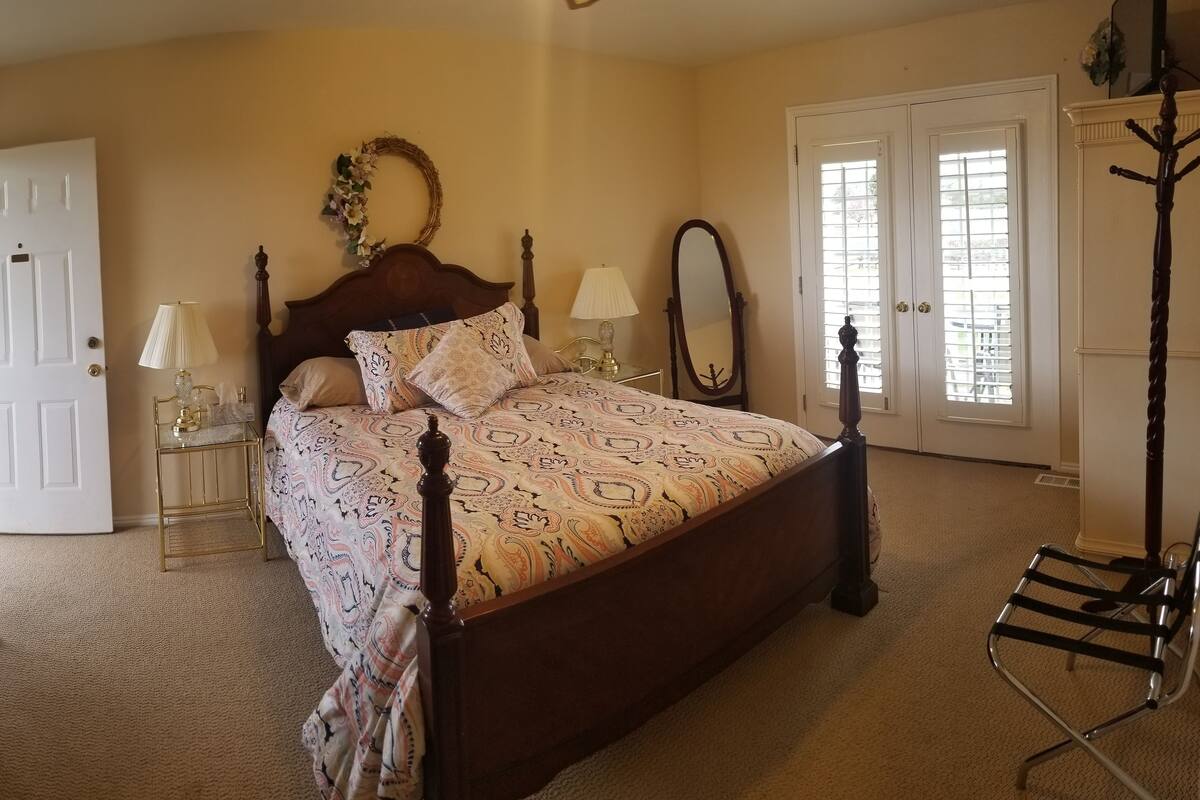 A bedroom with a four-poster bed, a bedside table with a lamp, a dresser with a mirror, and a coat rack.