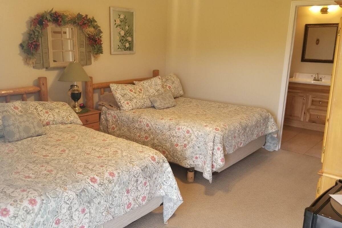 A bedroom with two single beds, a nightstand with a lamp, a mirror, and a bathroom visible through an open door.