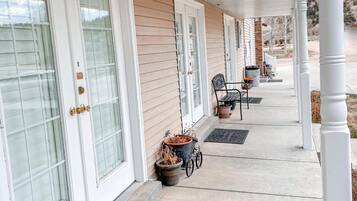 A covered porch with white columns, a wooden siding exterior, and a series of potted plants and a wheelbarrow.