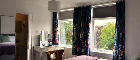 A bedroom with a bed, a desk, a chair, a dresser, and a window with curtains.