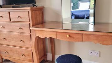 A wooden desk with a mirror, a television, and a small stool.