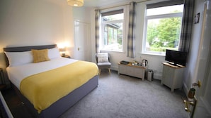 A hotel room with a bed, bedside table, chair, TV, and a window with curtains. - Atholl House Skye (Dunvegan)