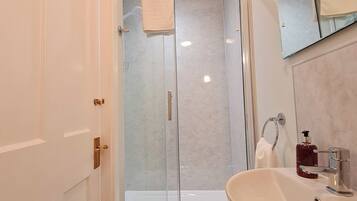 Un bagno moderno con box doccia in vetro, lavandino con dispenser di sapone e specchio sopra il lavandino.