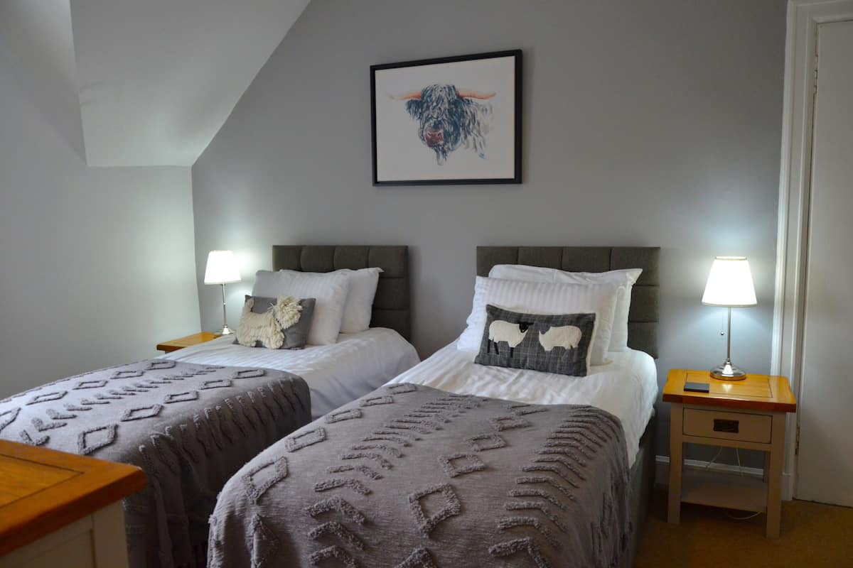 A room with two beds, each with a headboard, bedside tables, lamps, and a framed picture on the wall.