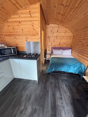 Een compacte kamer met een kitchenette, een bed en een klein nachtkastje.