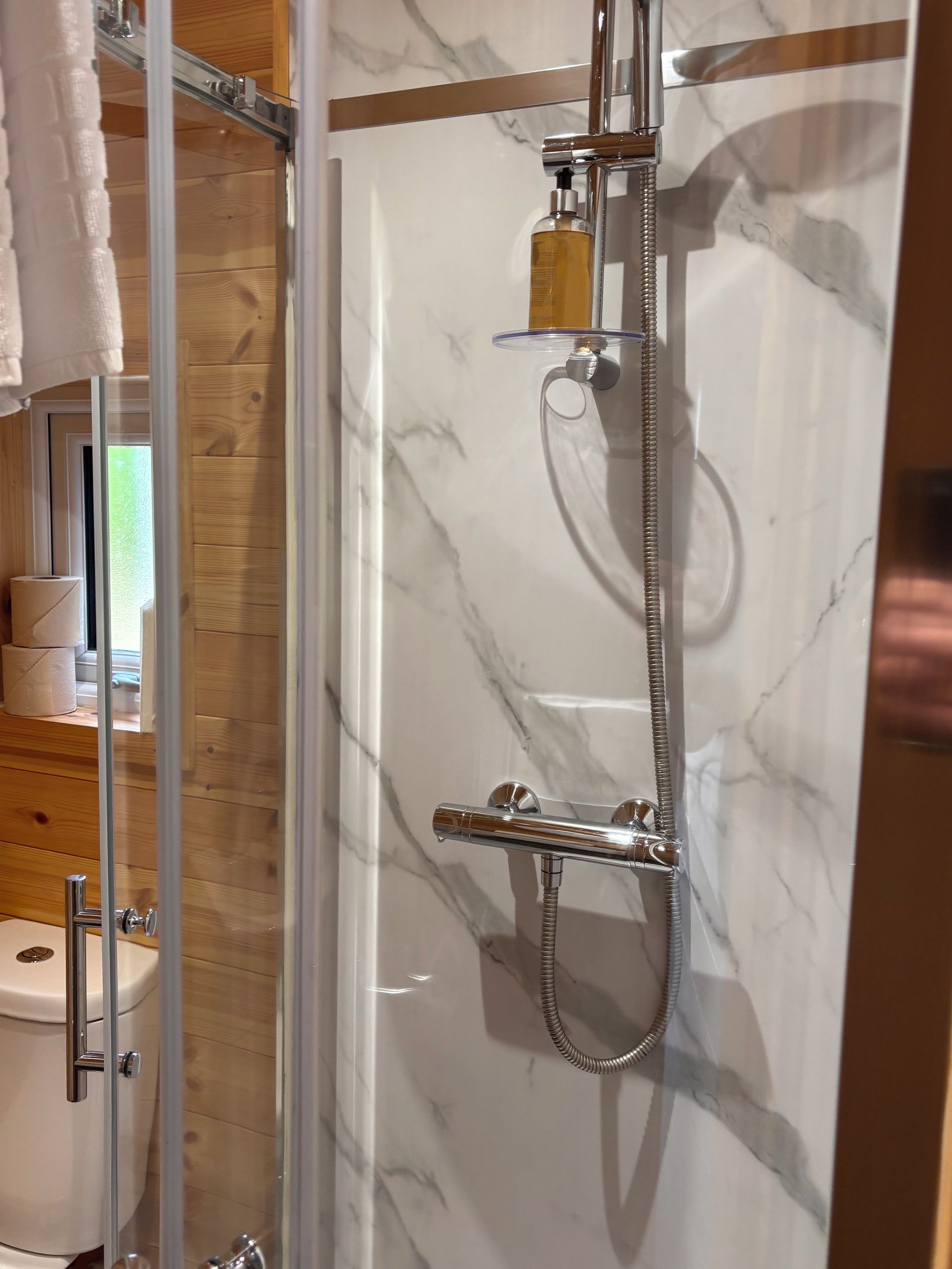 Un baño con cabina de ducha de vidrio, inodoro y tocador de madera con espejo.