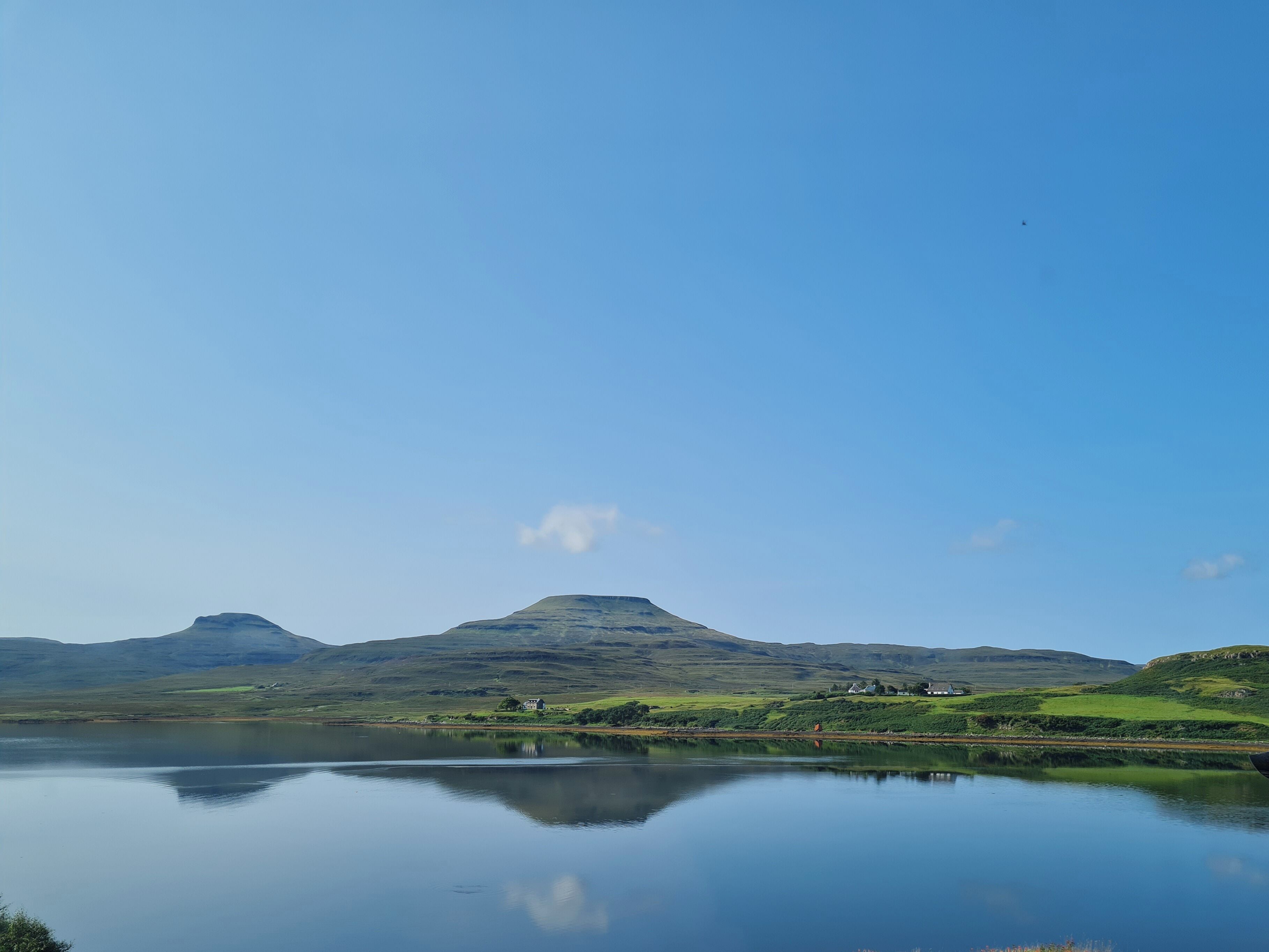 Um lago tranquilo com uma montanha ao fundo e alguns edifícios na margem.