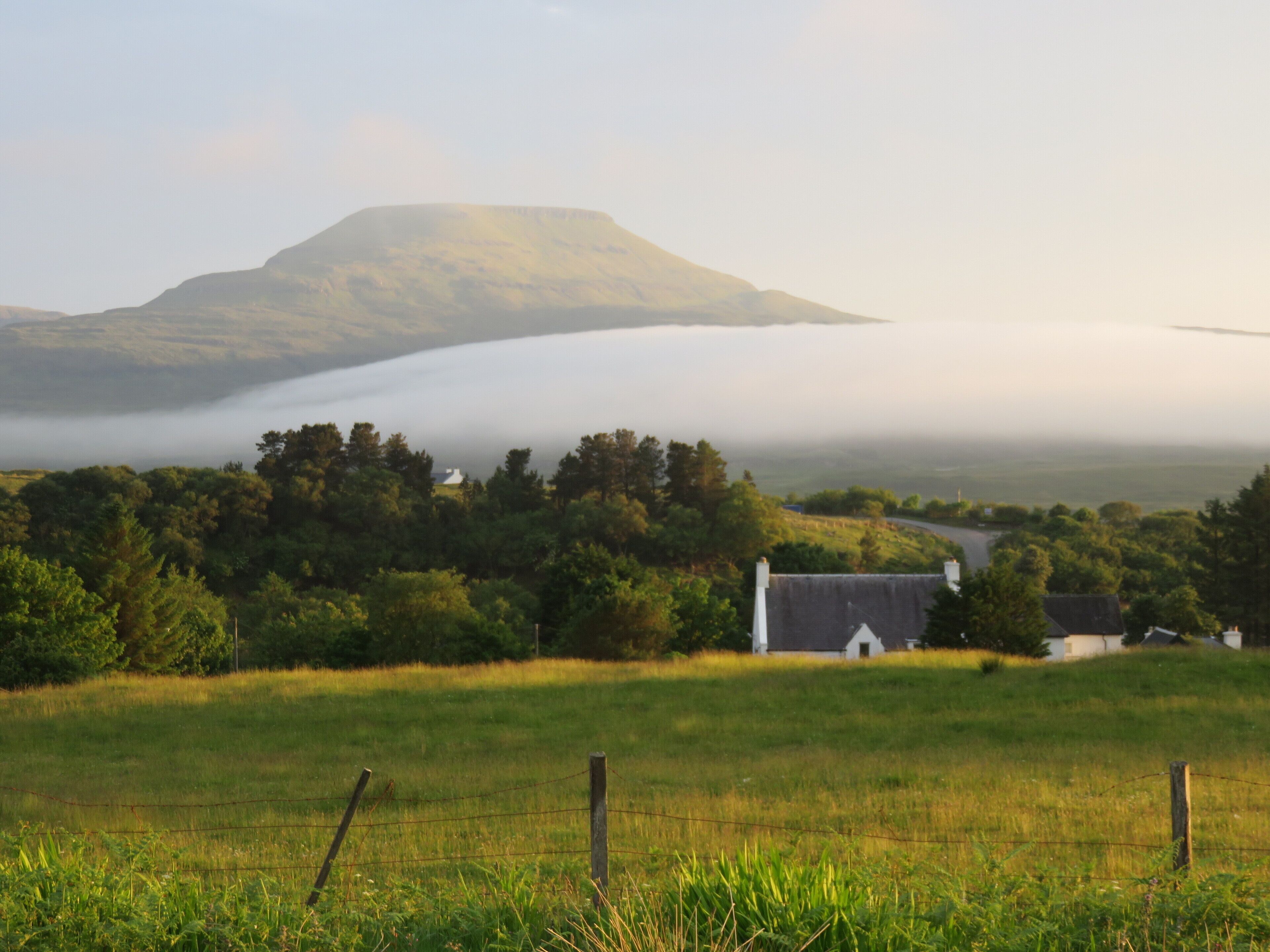 Un paysage rural avec une maison, une montagne et une vallée brumeuse.