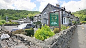 Ein traditionelles Steinhaus mit einem Schild für das Oakfield House B&B, das eine Steinmauer, einen Schotterweg und einen Parkplatz zeigt.
