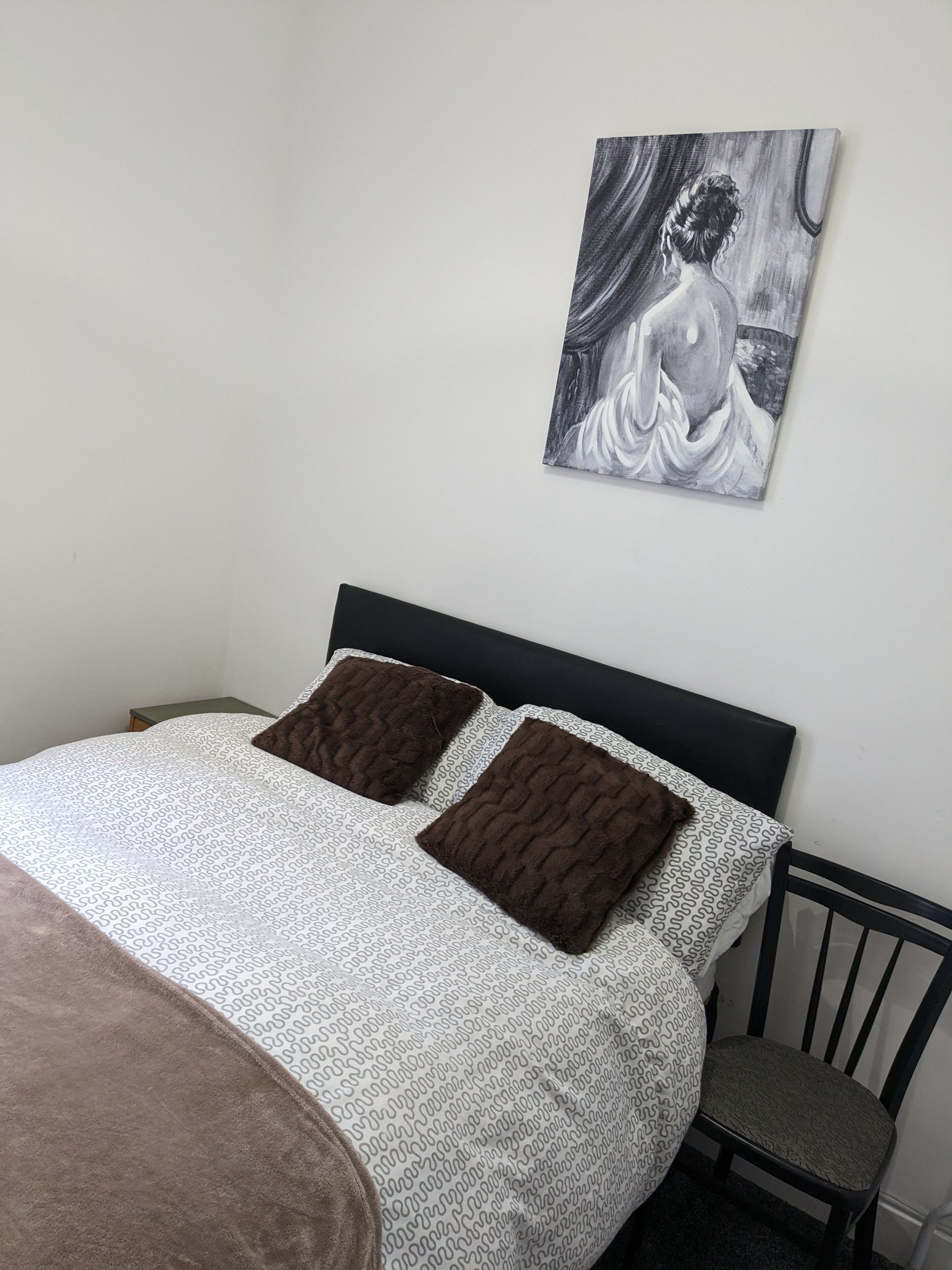 A bedroom with a bed, two pillows, a chair, and a wall-mounted painting.