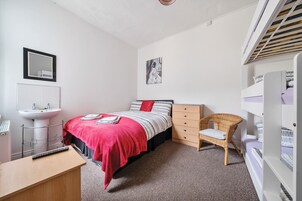Een slaapkamer met een bed, een bureau, een stoel, een dressoir, een kledingkast en een spiegel.
