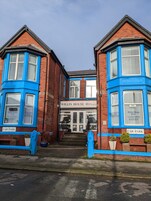 Een Willin House Hotel met een klassieke bakstenen gevel en blauwe accenten. Het heeft een centrale ingang met treden, een bordje dat een gratis parkeerplaats aangeeft, en een bord met de naam van het hotel op de begane grond.