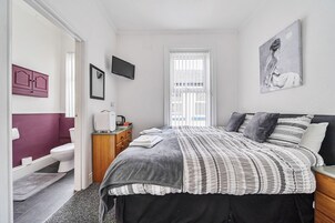 Een slaapkamer met een bed, een televisie, een raam en een zichtbare badkamer door een geopende deur.