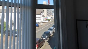 Una finestra con persiane verticali, vista su una strada con auto e una torre rossa in lontananza.