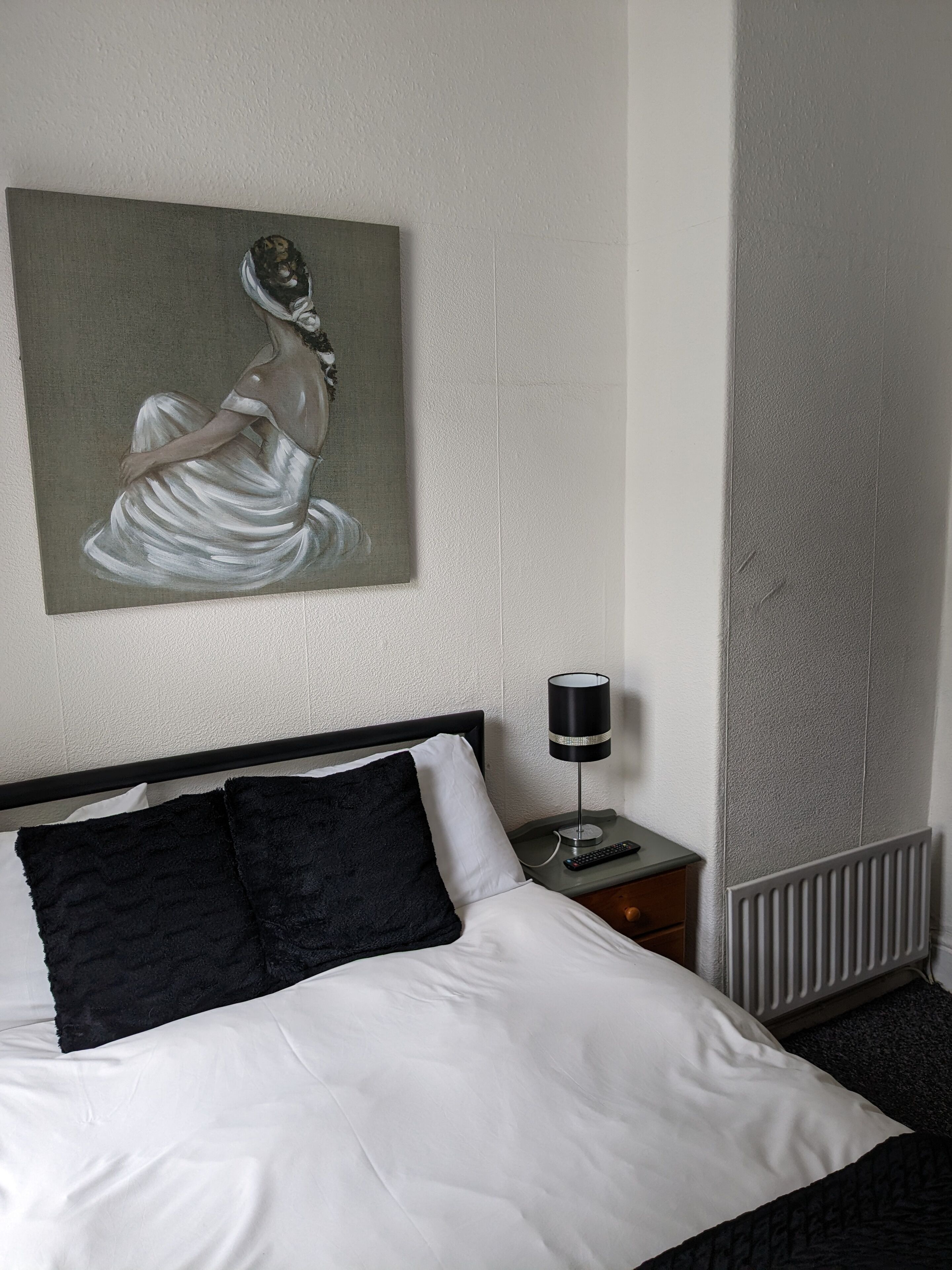 A hotel room with a bed, a painting, a nightstand, and a lamp.