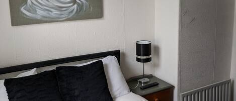 A hotel room with a bed, a painting, a nightstand, and a lamp.
