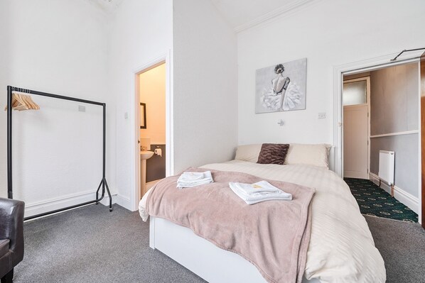 A bedroom with a bed, a wardrobe, a radiator, and a door leading to another room.