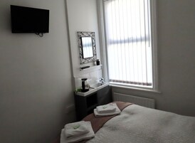 A hotel room with a bed, a TV mounted on the wall, a bathroom with a sink and mirror, and a window with blinds.