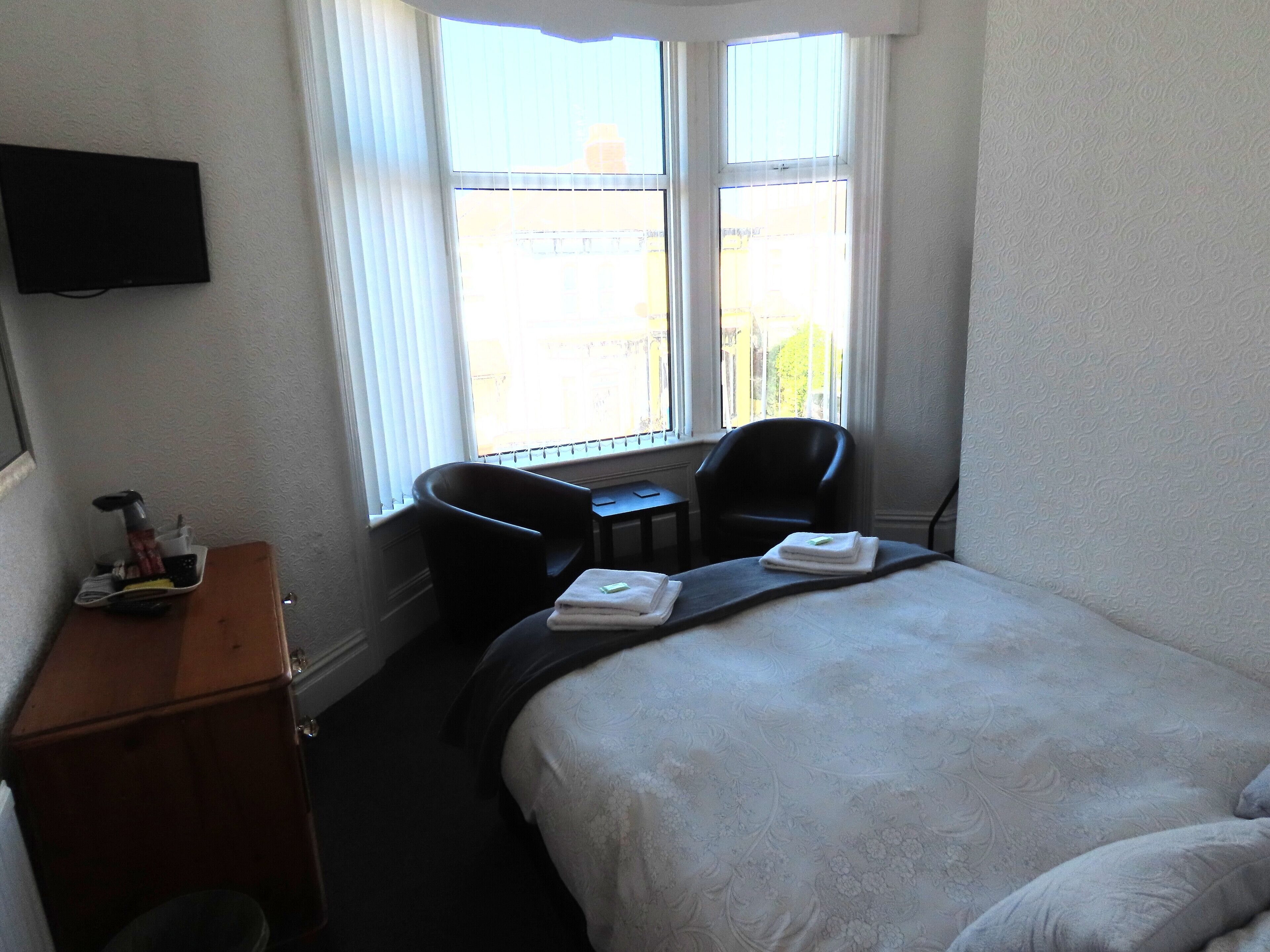 Una habitación de hotel con cama, escritorio, silla y televisor en la pared.