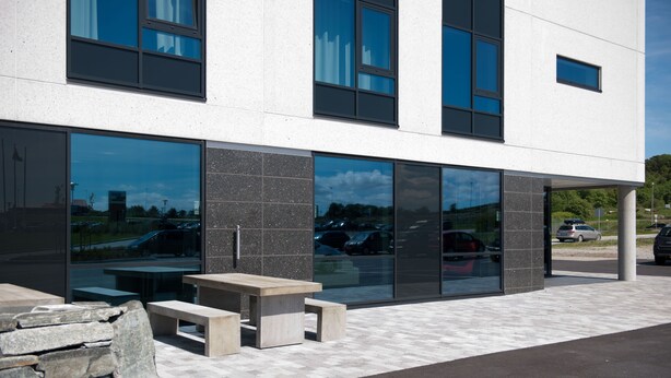 A modern building with large windows, outdoor seating, and a stone wall. - Tananger Apartment Hotel  (Sola)