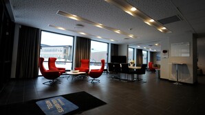 A modern hotel lobby with a reception desk, seating area with red chairs, large windows, and a view of the cityscape. - Tananger Apartment Hotel  (Sola)