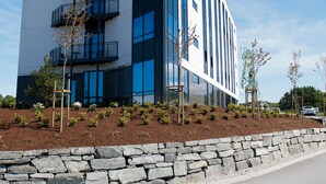 A modern building with a white facade, multiple balconies, and a stone retaining wall. - Tananger Apartment Hotel  (Sola)