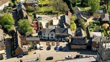 An aerial view of a village with a central pub, surrounded by residential buildings and a parking area.