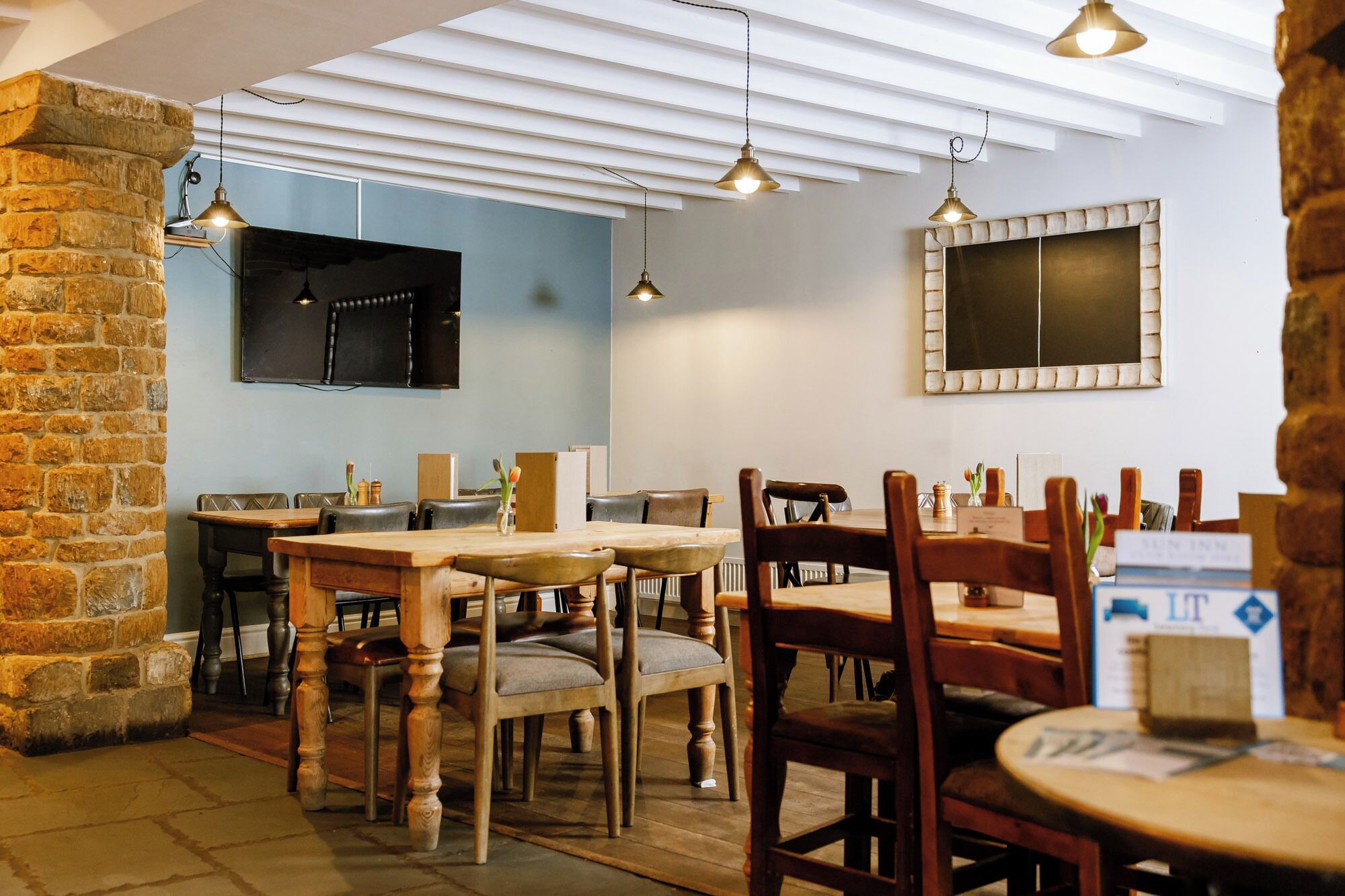Ein gemütliches Restaurant mit Holztischen und -stühlen, einer Steinwand und Pendelleuchten.