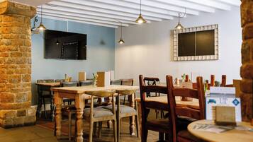 Un restaurante acogedor con mesas y sillas de madera, un muro de piedra e iluminación colgante.