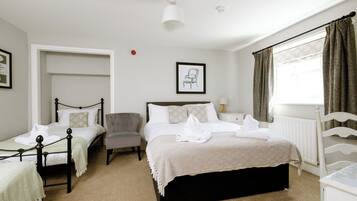 A hotel room with a large bed, two smaller beds, a chair, a desk, and a window with curtains.