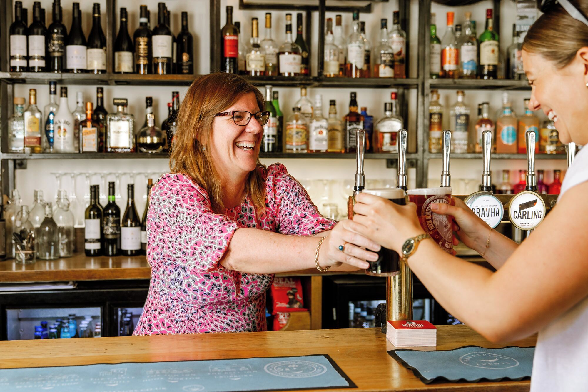 A bar with shelves of various liquor bottles and a person pouring a drink.