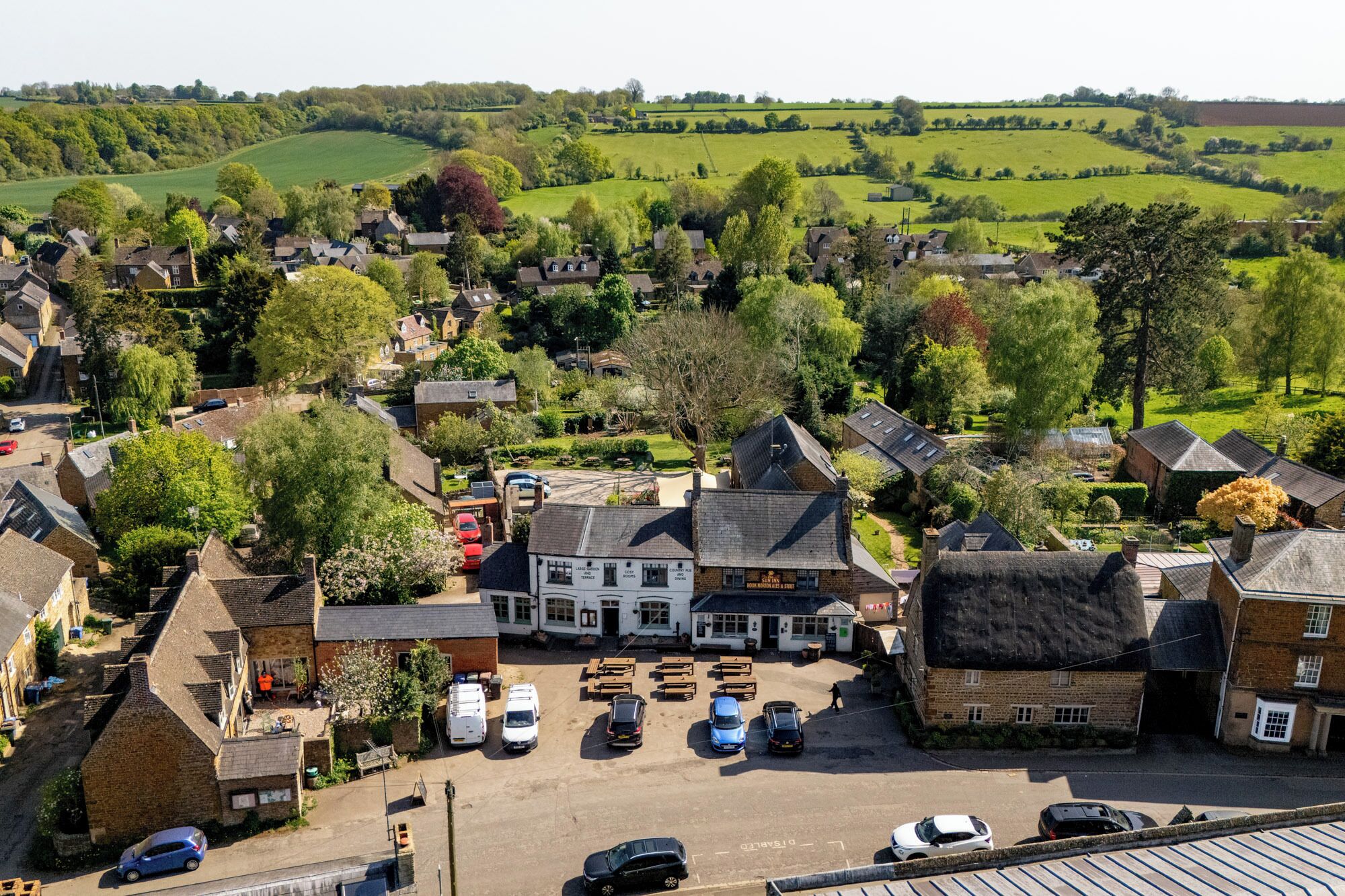 A village with a central pub, surrounded by residential buildings and open fields.