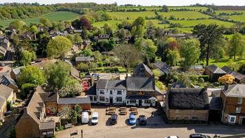 A village with a central pub, surrounded by residential buildings and open fields.