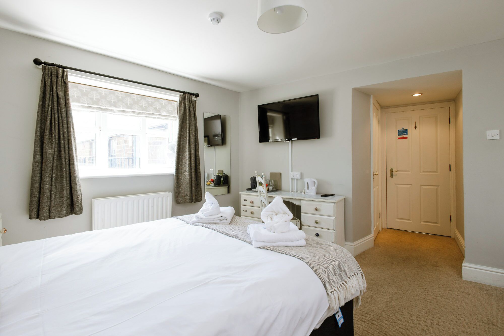 A hotel room with a bed, a desk, a flat-screen TV, a radiator, and a door.