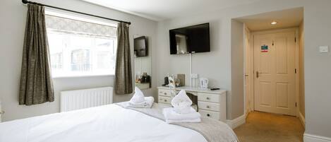 A hotel room with a bed, a desk, a flat-screen TV, a radiator, and a door.