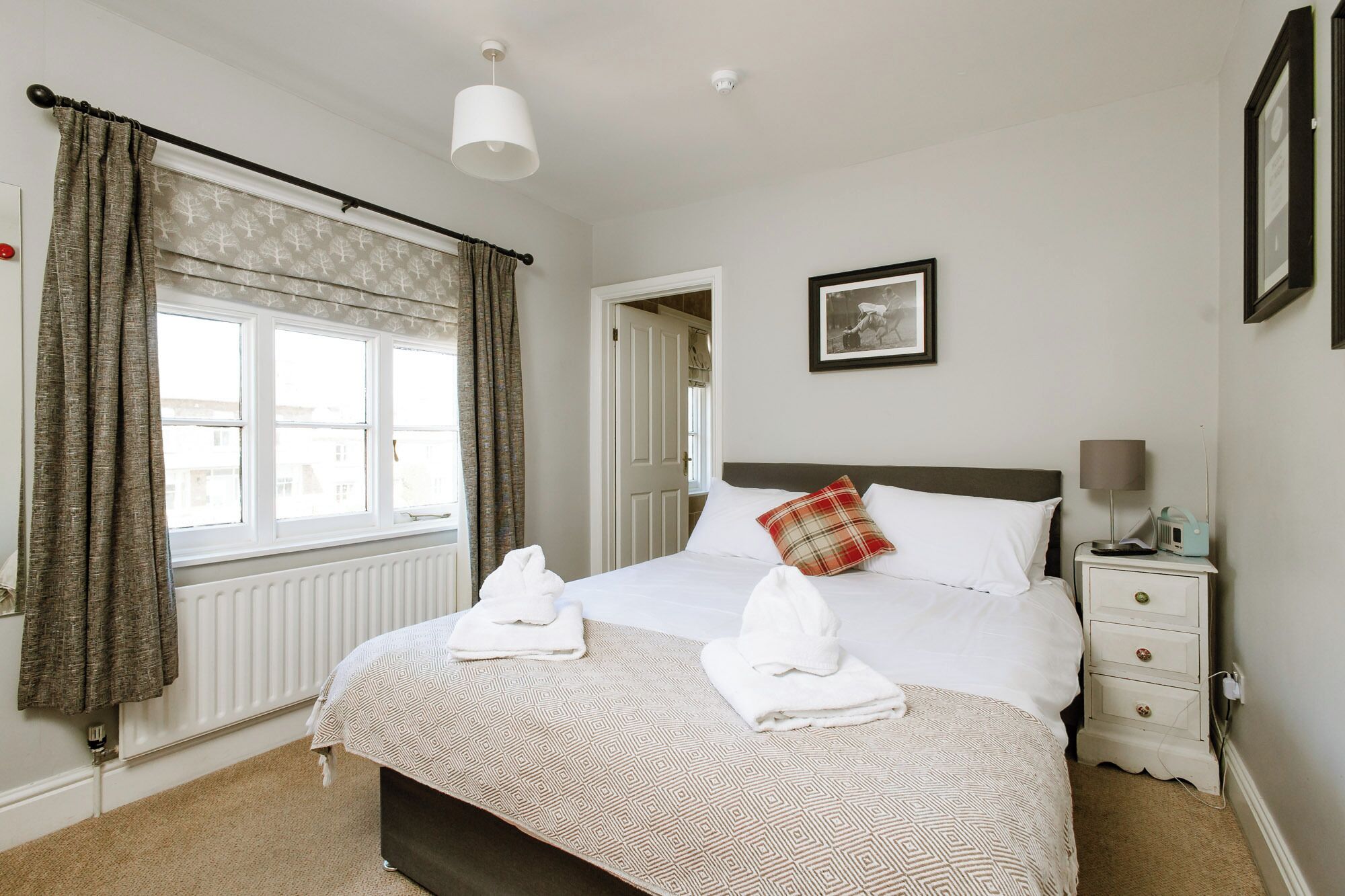 A neatly arranged bedroom with a bed, bedside table, lamp, and a framed picture on the wall.