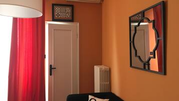 Una habitación con una puerta, un radiador, un espejo sujeto a la pared y una cortina roja.