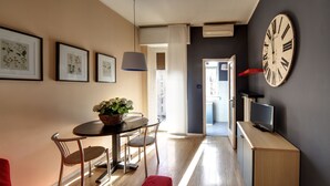 Una sala de estar moderna con comedor, un reloj de pared grande e impresiones botánicas enmarcadas.